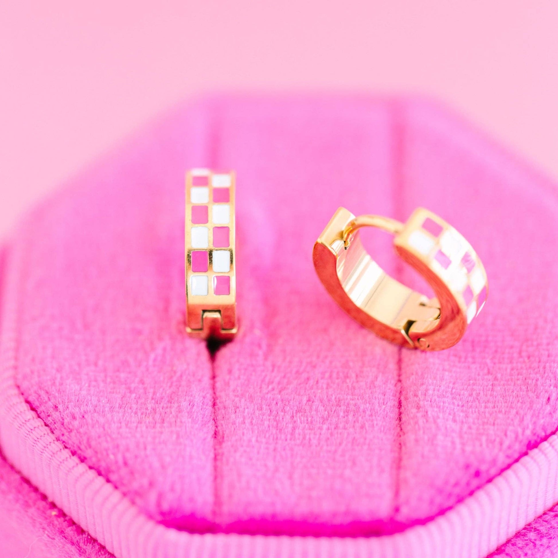 Two gold pink checkered hoop earrings on a pink textured surface