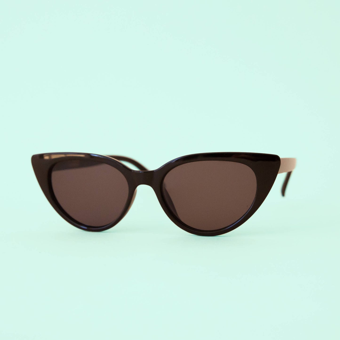 Cat-eye sunglasses with brown lenses on a light green background
