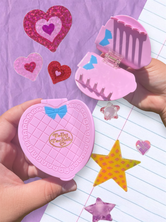 Pink polly pocket compact mirror and hair clip held over a notebook with stickers.