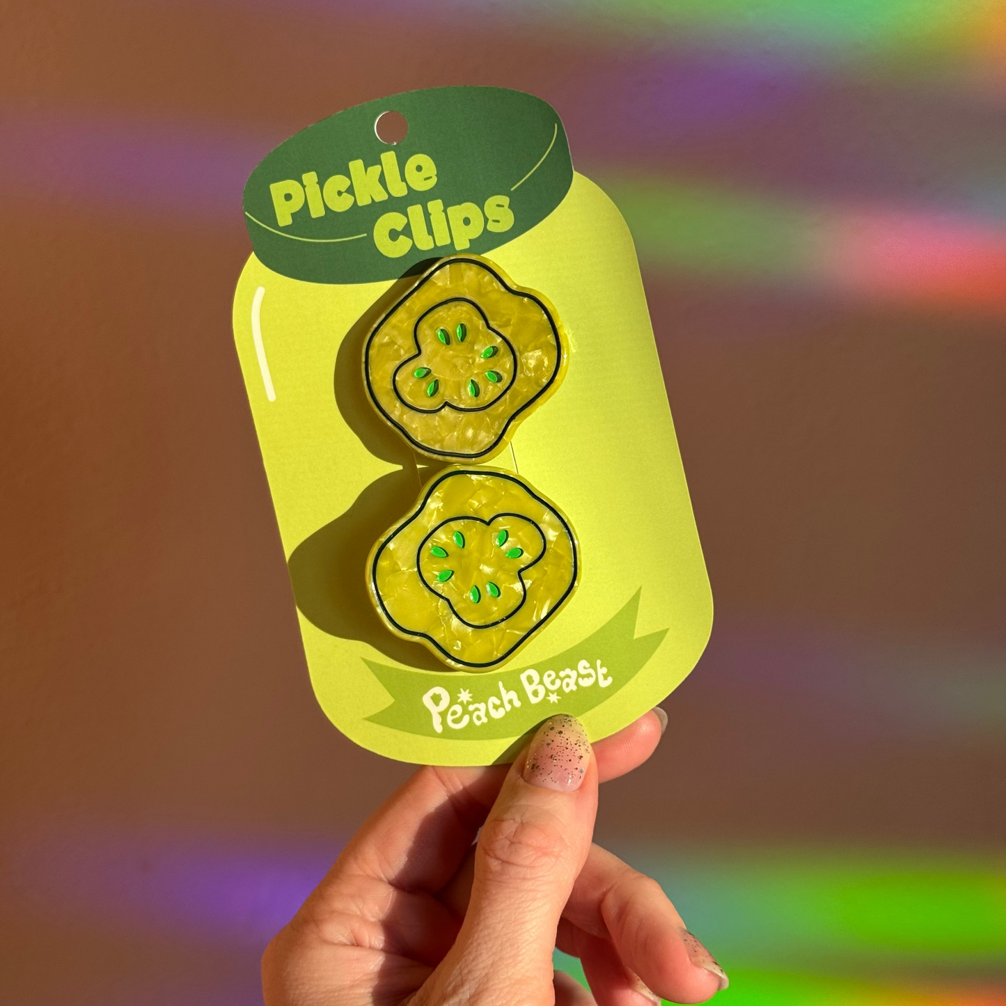Pickle-shaped clips in packaging held by a hand with a colorful background