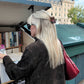 Person with long blonde hair and sunglasses looking at books from a table outdoors with a Small book claw clip