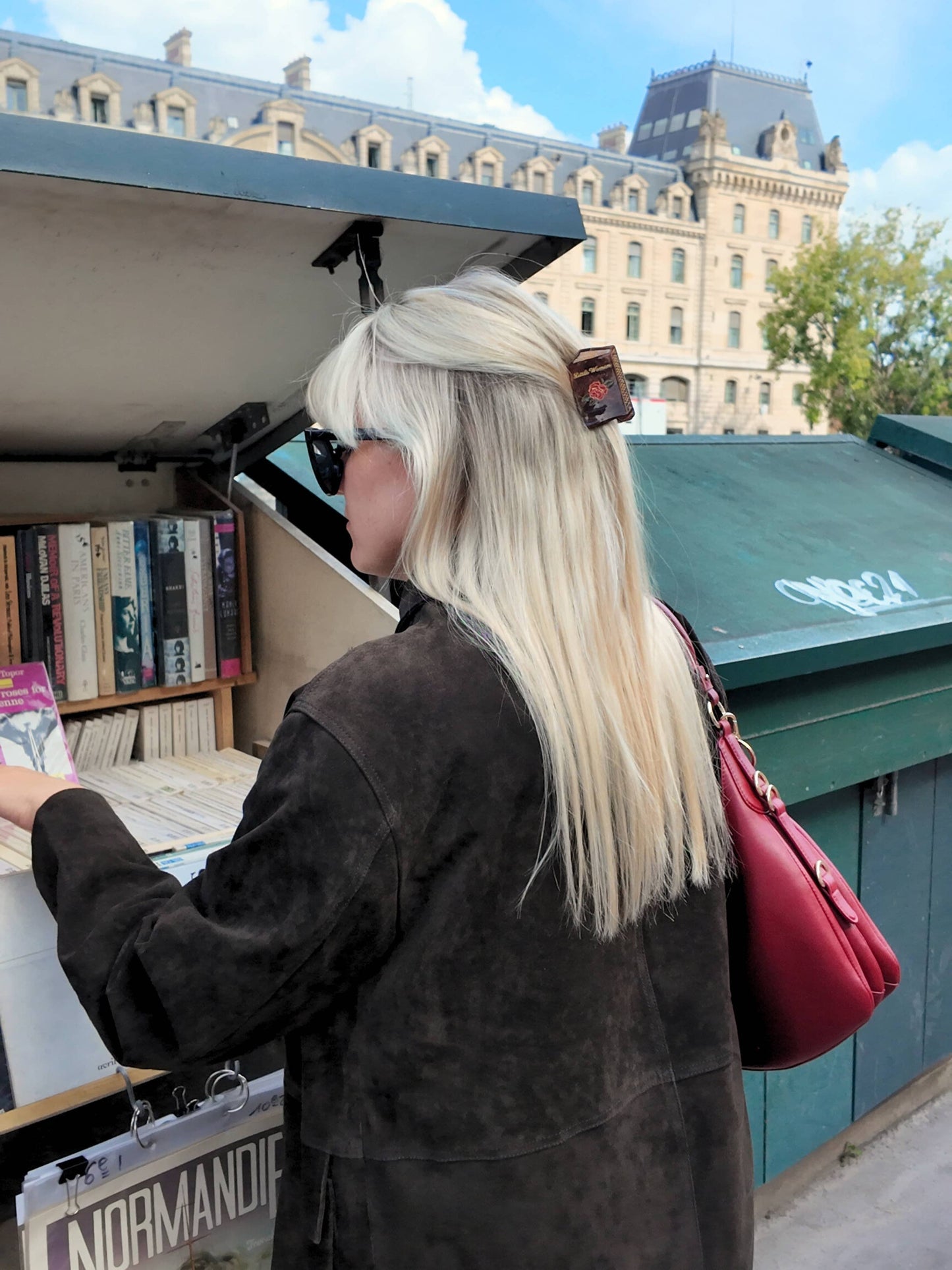 Person with long blonde hair and sunglasses looking at books from a table outdoors with a Small book claw clip