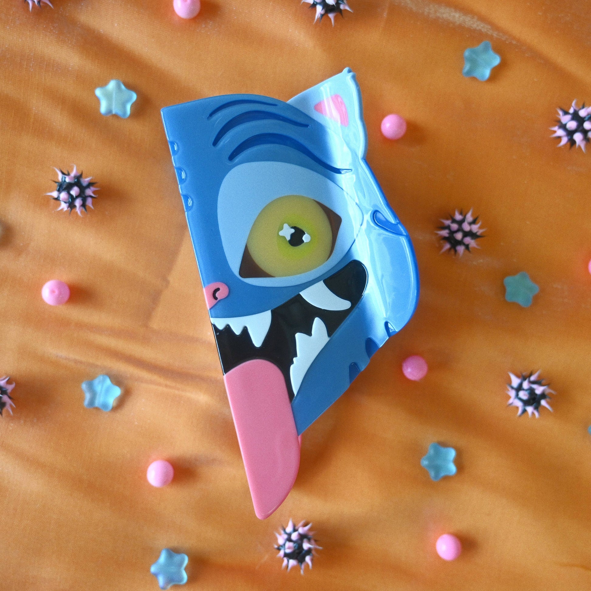 Blue tiger hair claw with a pink tongue on an orange background with colorful shapes