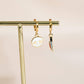 Gold earrings with skull and knife charms on a beige background