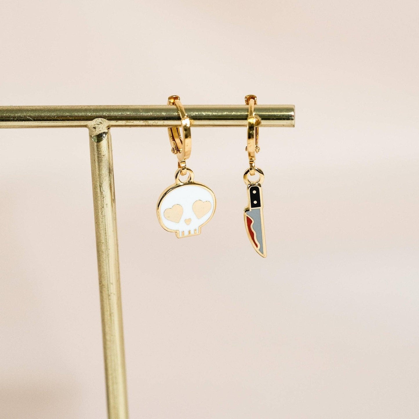 Gold earrings with skull and knife charms on a beige background
