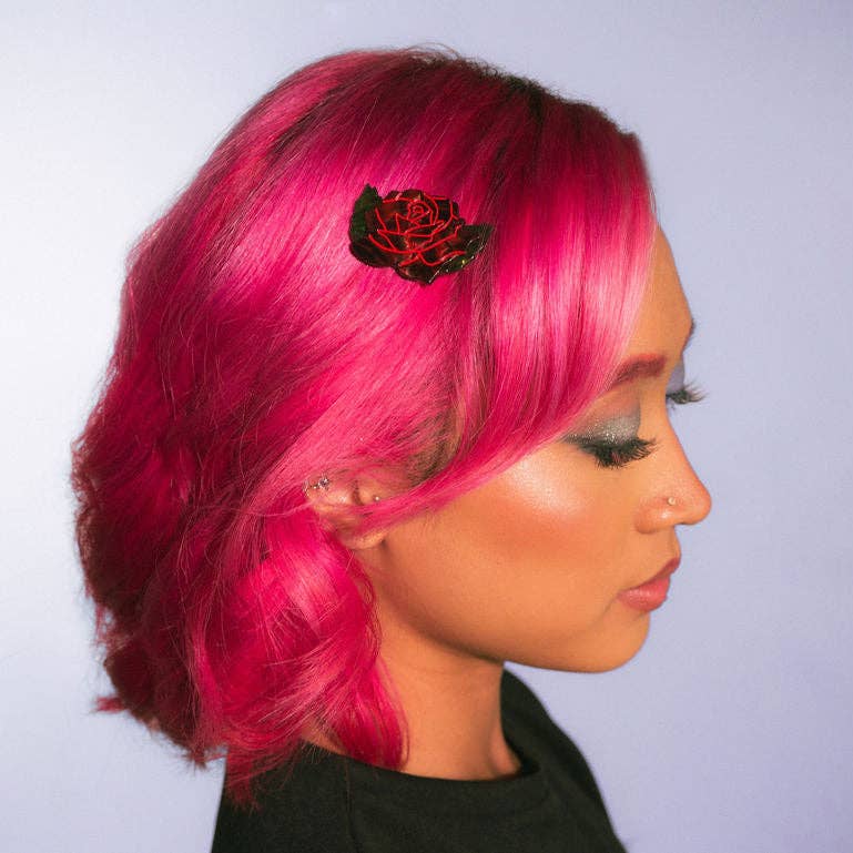 Person with bright pink hair wearing a rose hair clip against a light gray background