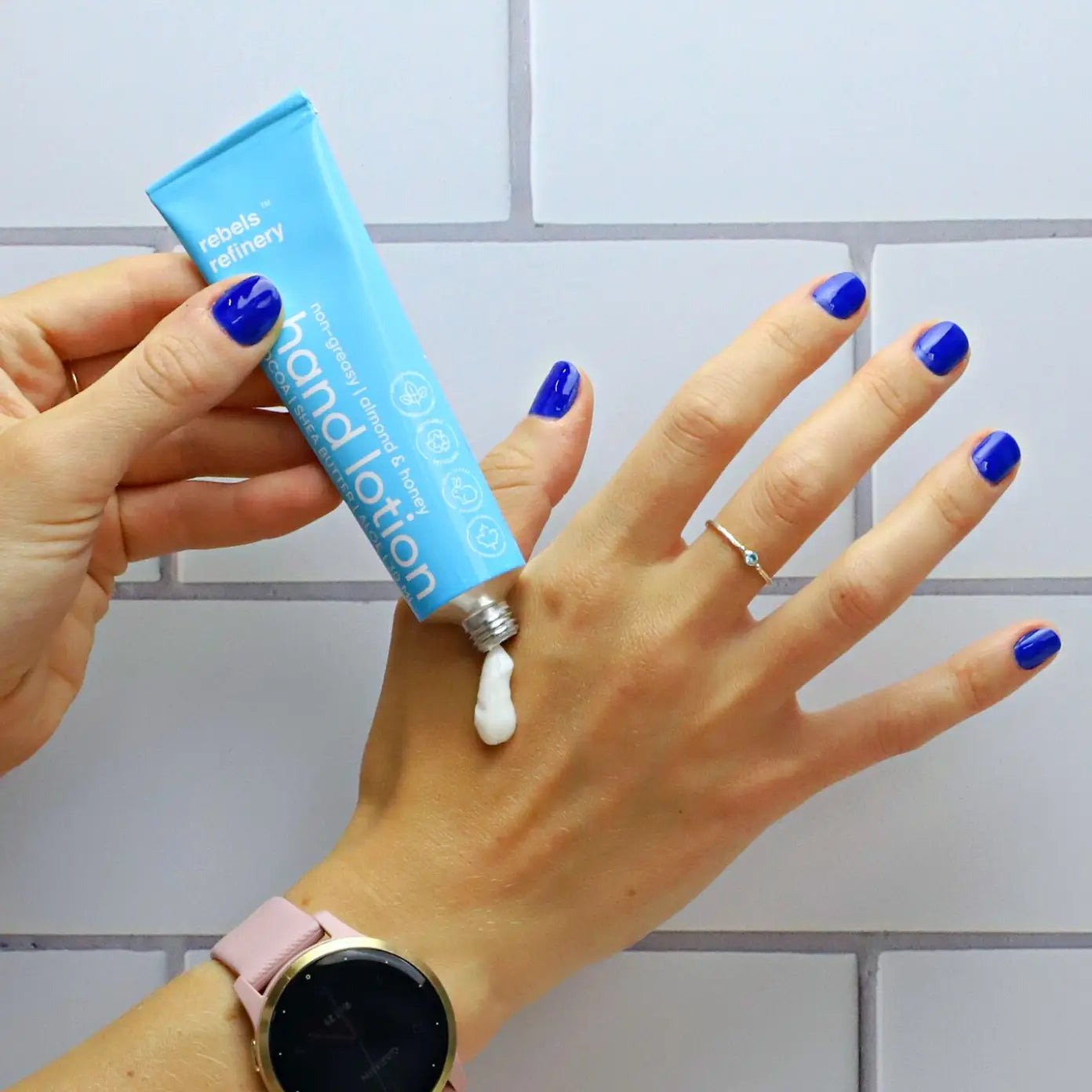Hand applying hand lotion to a wrist with a tiled bathroom background