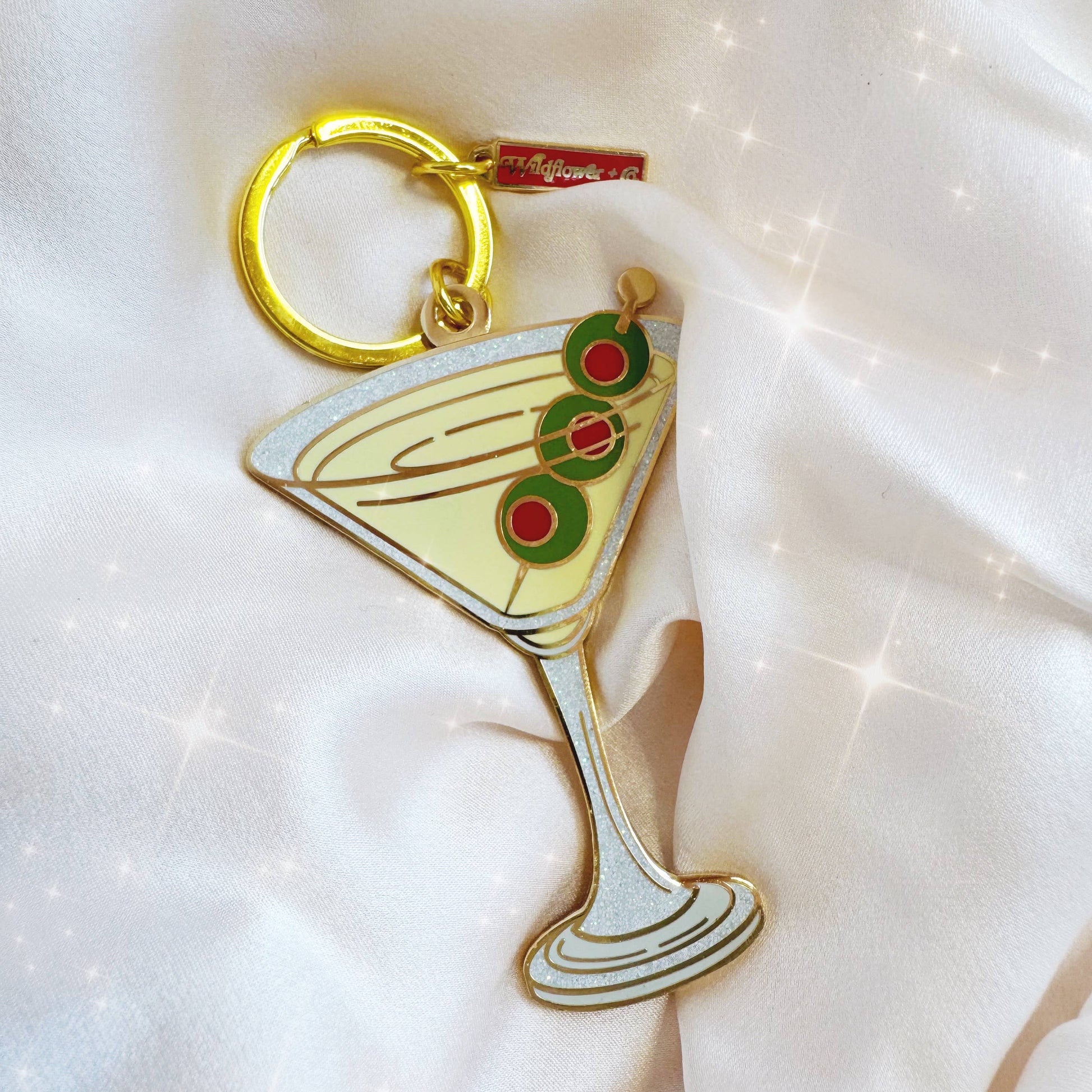 Keychain shaped like a martini glass with olives on a white background