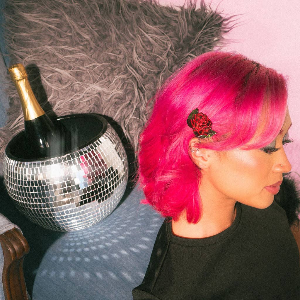 Person with pink hair and a rose flower in their hair next to a disco ball and bottle.
