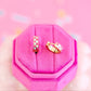 Two gold pink checkered hoop earrings on a pink hexagonal jewelry box.