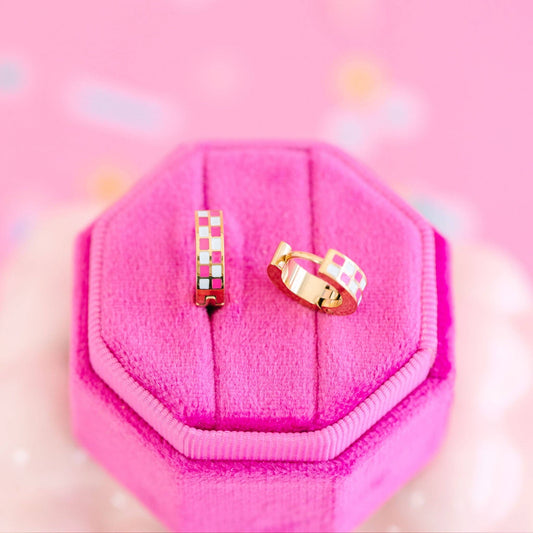 Two gold pink checkered hoop earrings on a pink hexagonal jewelry box.