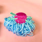 Blue yarn ball with a pink knitting yarn claw clip and green sticks on a pink background