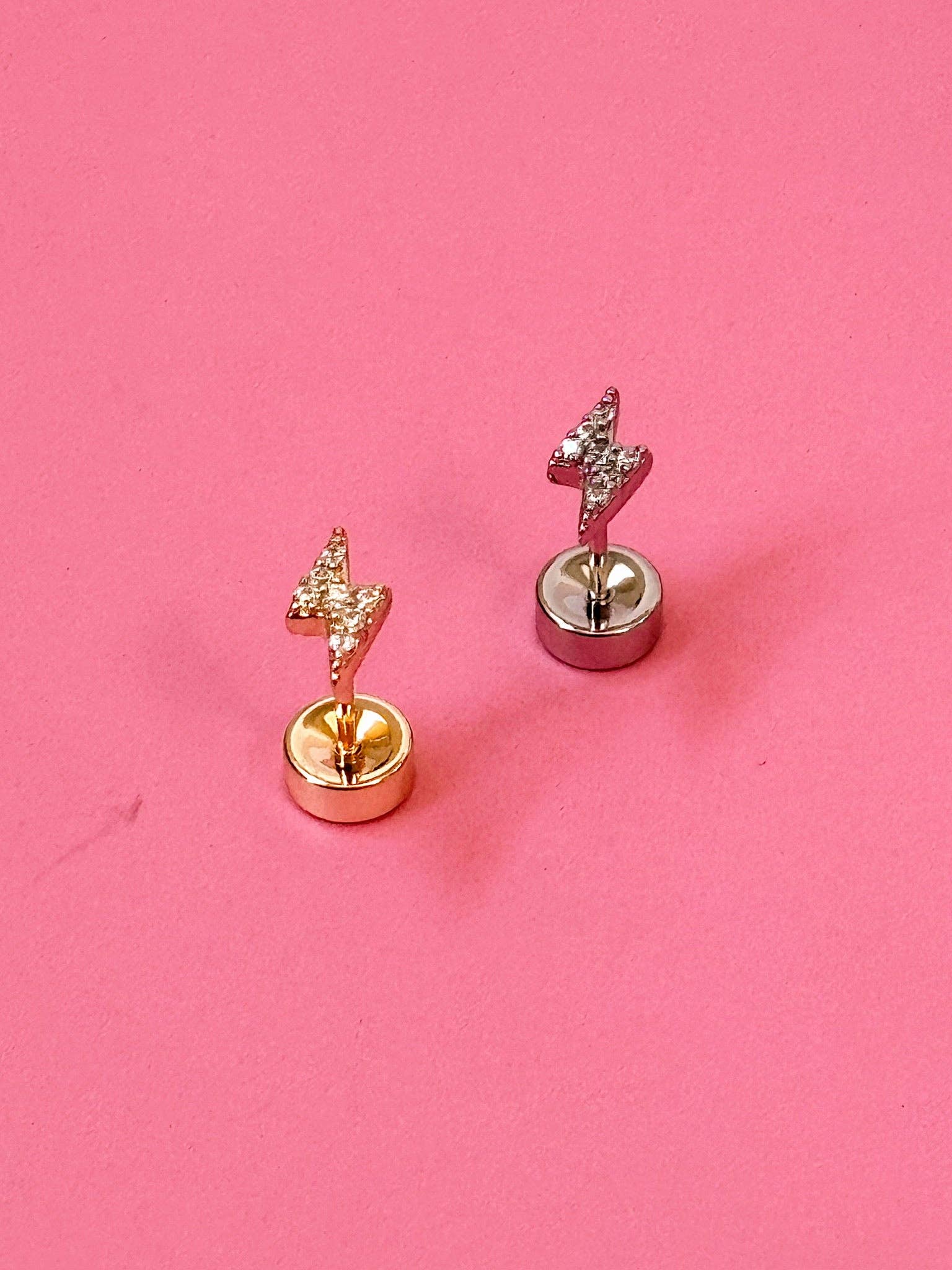 Pair of gold and silver lightening bolt stud earrings on a pink background
