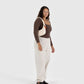 Woman wearing a brown top, beige apron, and white pants on a white background