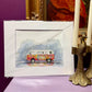 Colorful van illustration in a white frame on a purple surface with candles and decorative items.