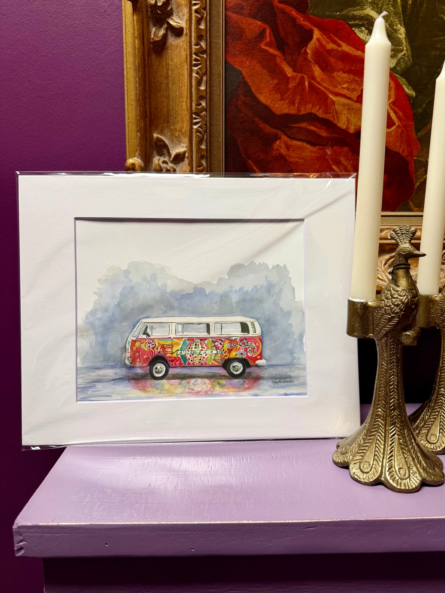 Colorful van illustration in a white frame on a purple surface with candles and decorative items.