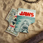 Two 'Jaws' playing cards on a sandy surface with a rope.