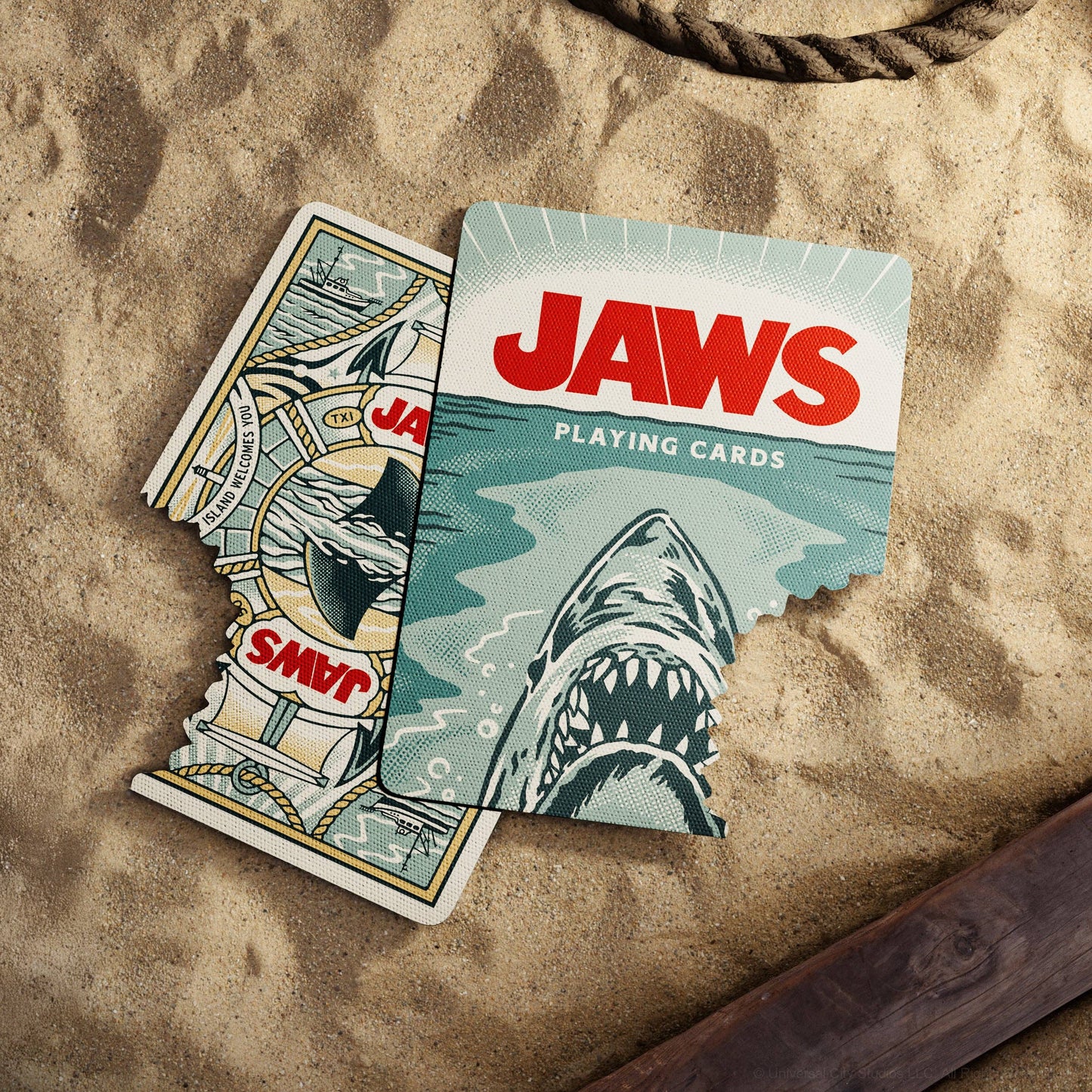 Two 'Jaws' playing cards on a sandy surface with a rope.