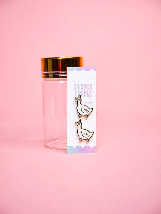 Clear bottle with gold cap and geese earrings on a pink background