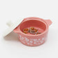 Pink jewelry box with floral patterns containing two rings on a white background