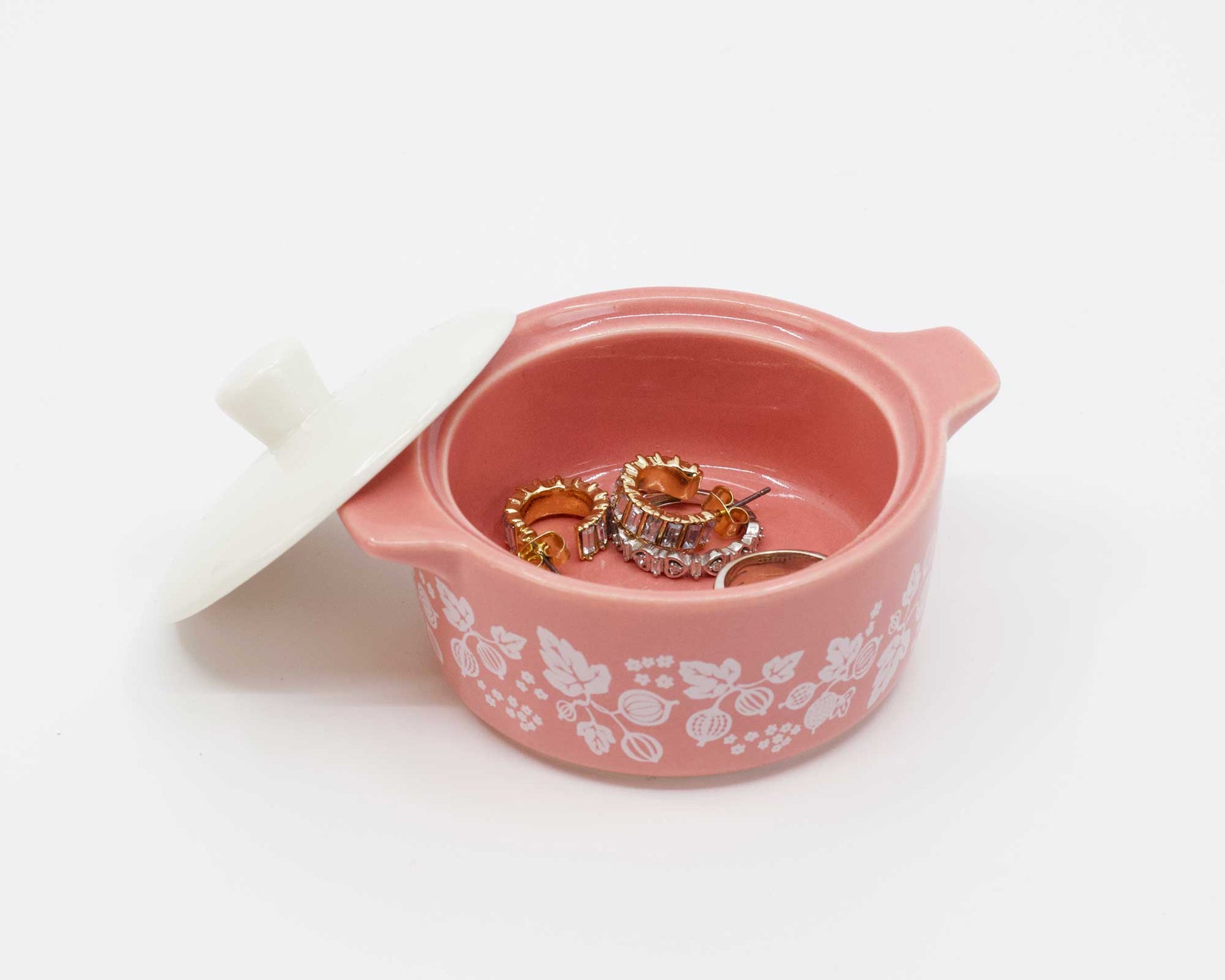 Pink jewelry box with floral patterns containing two rings on a white background