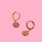 Gold hoop earrings with sunray-shaped charms on a pink background