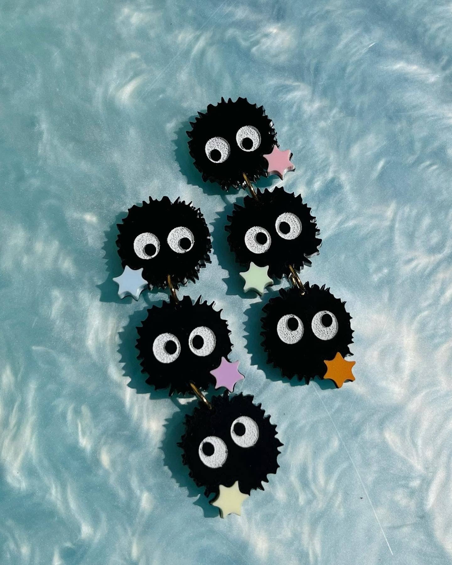 Set of soot sprites earrings on a light blue textured background