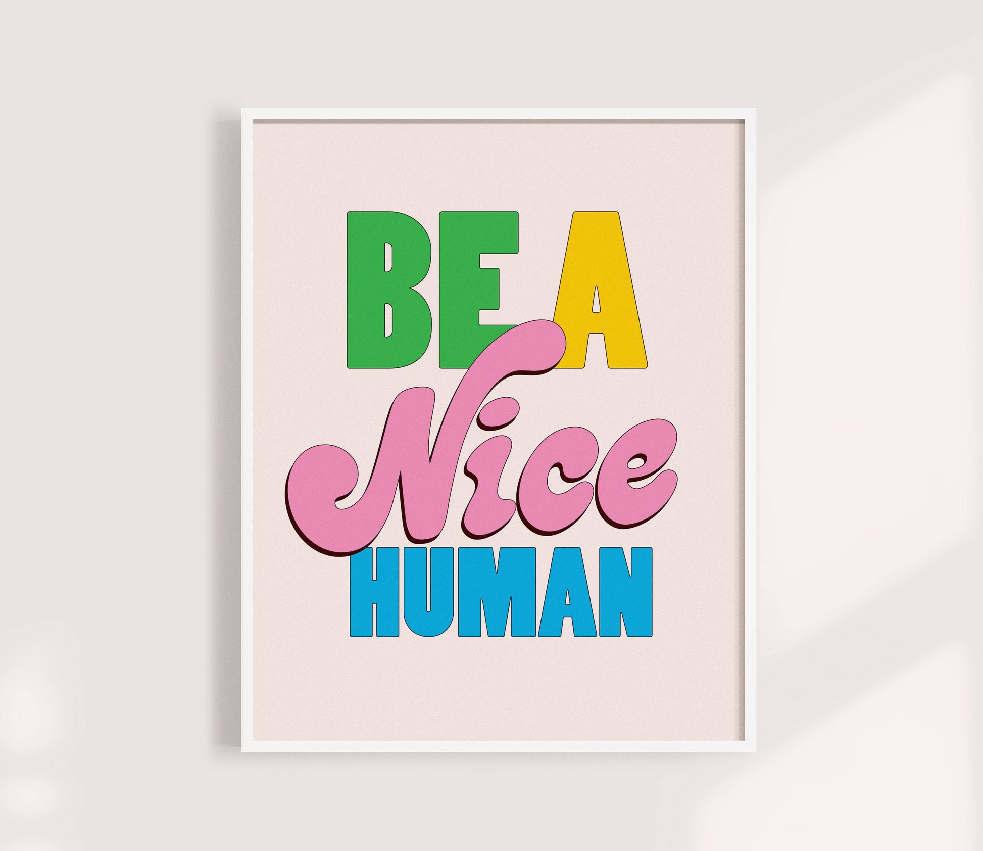 Framed poster with colorful text 'Be a Nice Human' on a light pink background