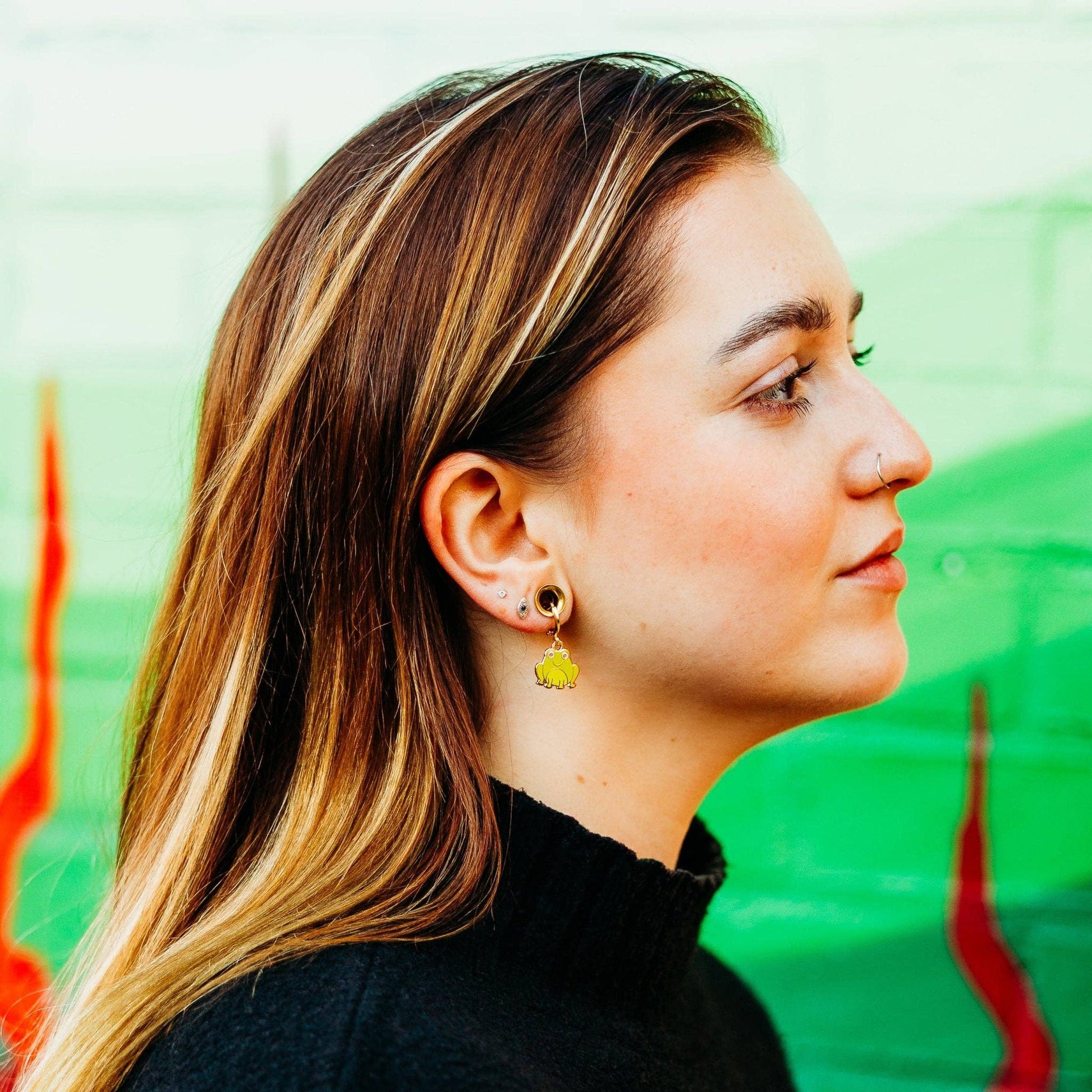 Woman wearing a yellow frog earring with a colorful abstract background