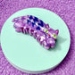 Purple hair clip on a round green platform with a purple textured background