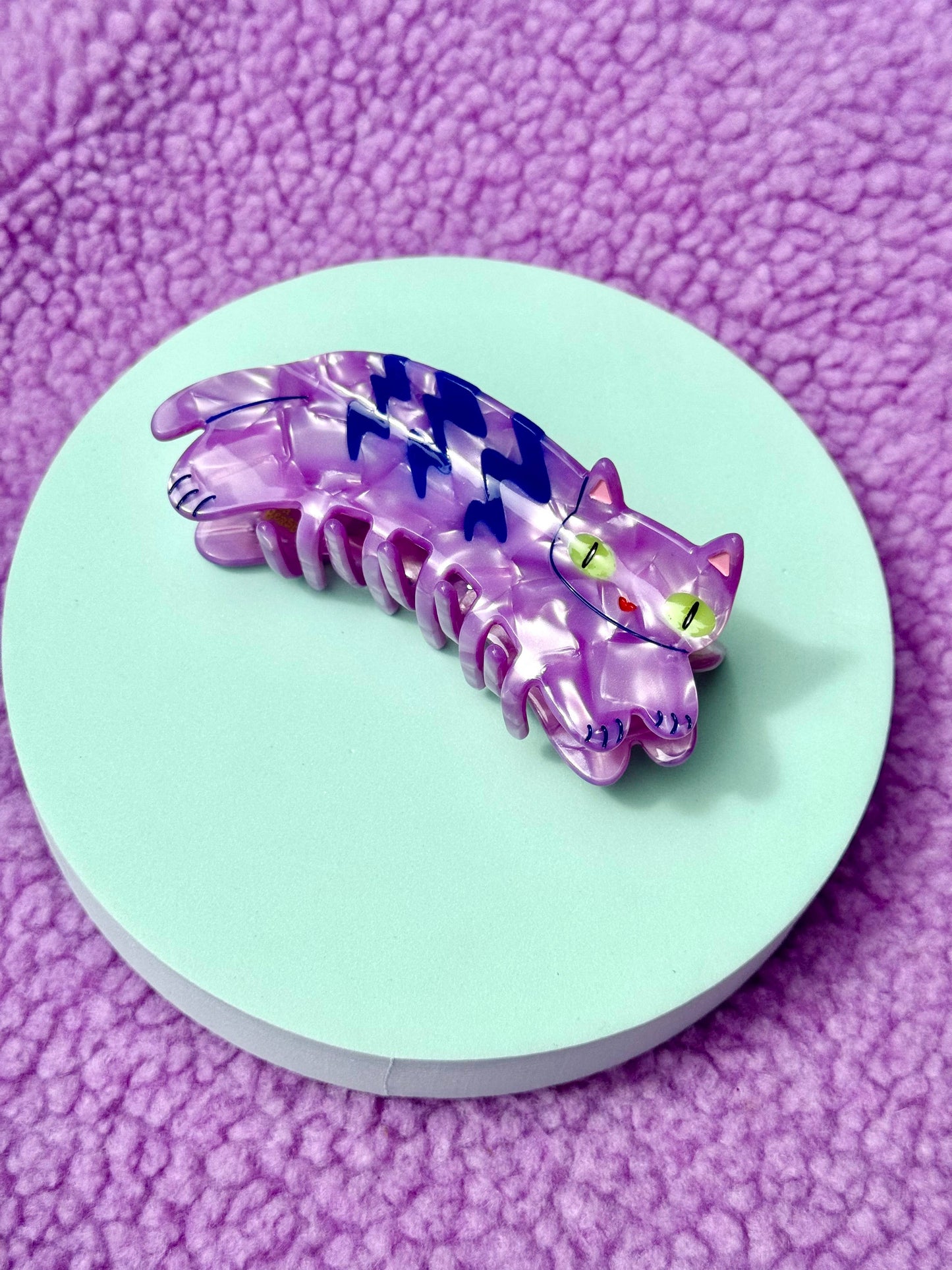 Purple hair clip on a round green platform with a purple textured background