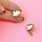 Cloud-shaped earrings with gold accents held by a hand on a pink background