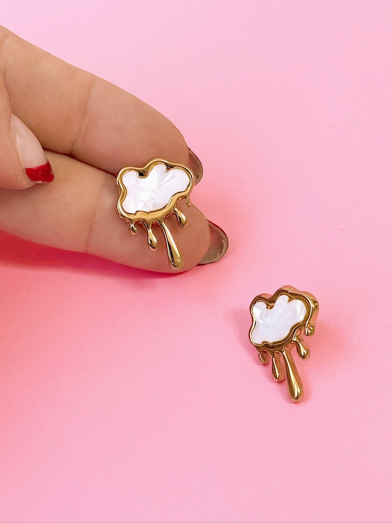 Cloud-shaped earrings with gold accents held by a hand on a pink background