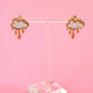 Pair of cloud-shaped earrings on a clear stand against a pink background