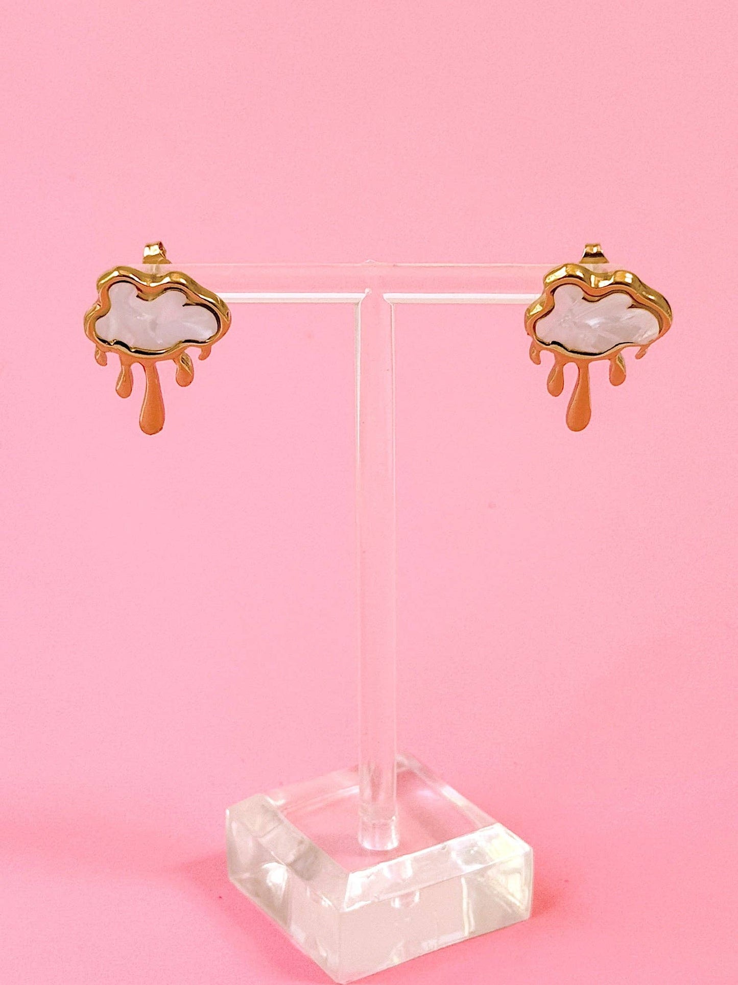 Pair of cloud-shaped earrings on a clear stand against a pink background