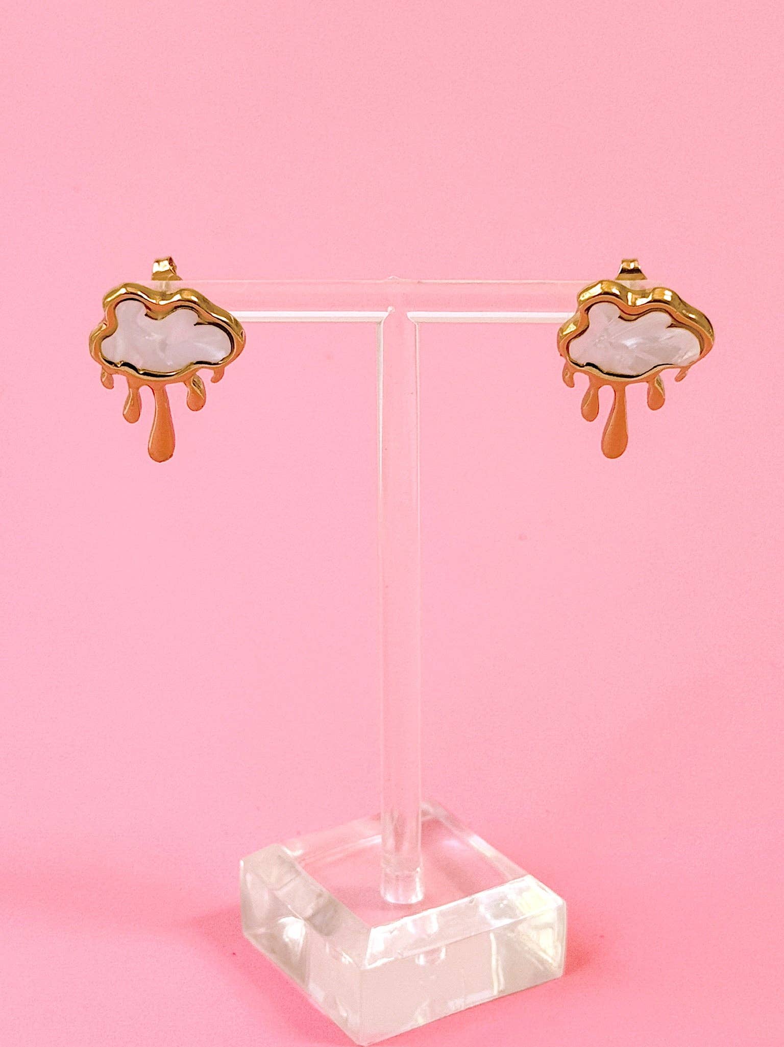 Pair of cloud-shaped earrings on a clear stand against a pink background