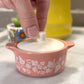 Pink pyrex ceramic container with floral patterns on a white surface