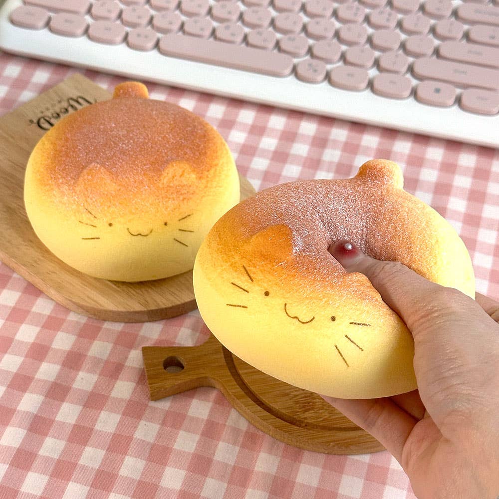 Two cat-shaped bread squishies on a checkered tablecloth with a hand holding one.