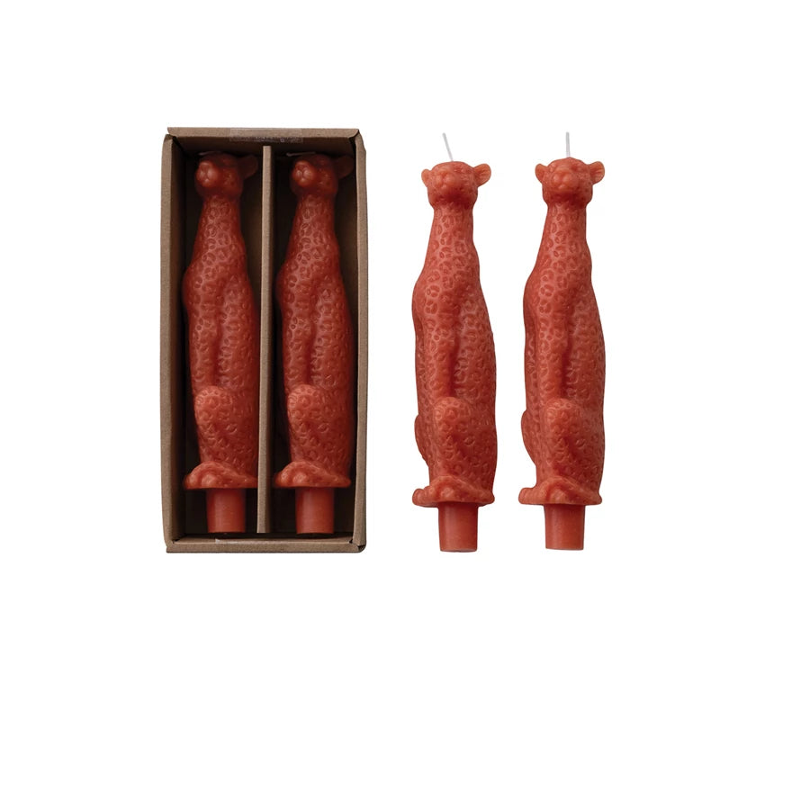 Two standing orange leopard-shaped candles with a box containing two more candles on a white background.