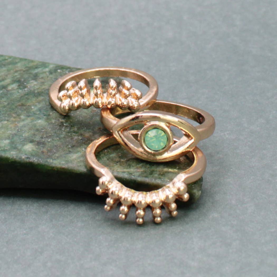 Three gold rings with gemstones on a green stone surface