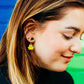 Close-up of a person wearing a yellow flower-shaped earring with a blurred background