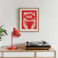 Turntable on a wooden shelf with a red lamp and framed poster on the wall.