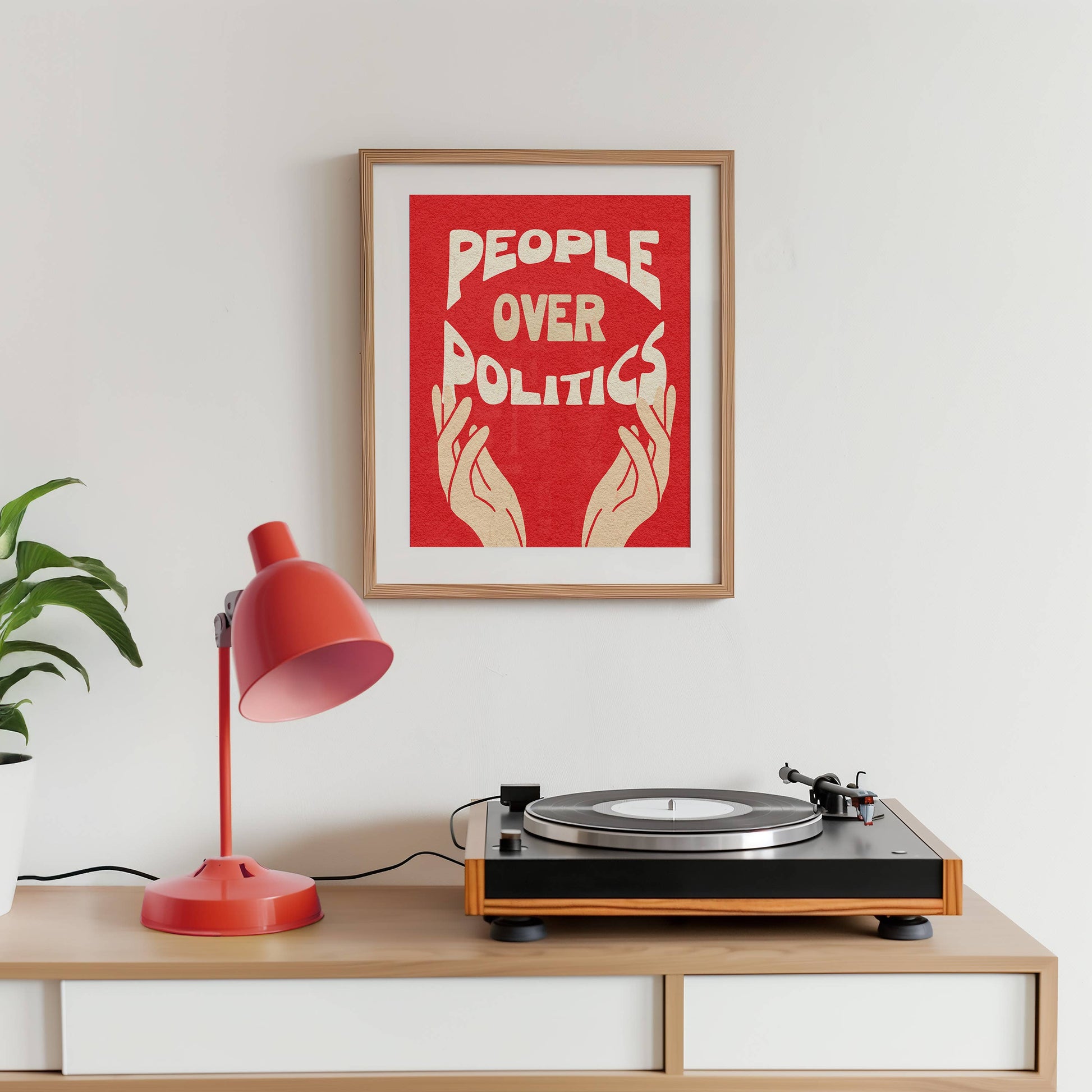 Turntable on a wooden shelf with a red lamp and framed poster on the wall.
