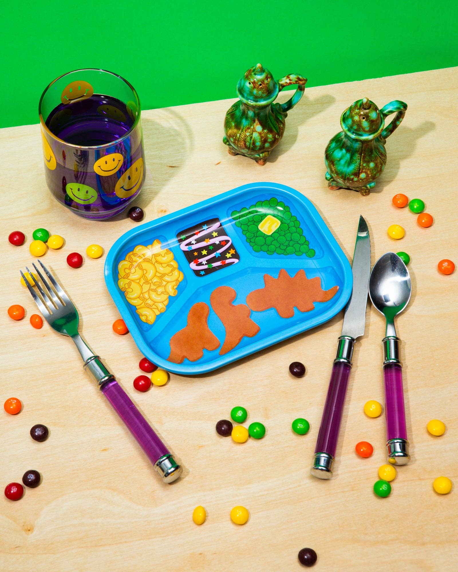 Children's table setting with colorful plate, cutlery, and snacks on a wooden surface.