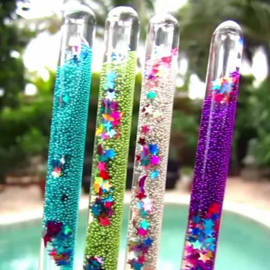 Four colorful beaded sticks with star patterns against a blurred natural background