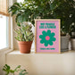 Framed artwork with a flower design and text on a windowsill with plants.