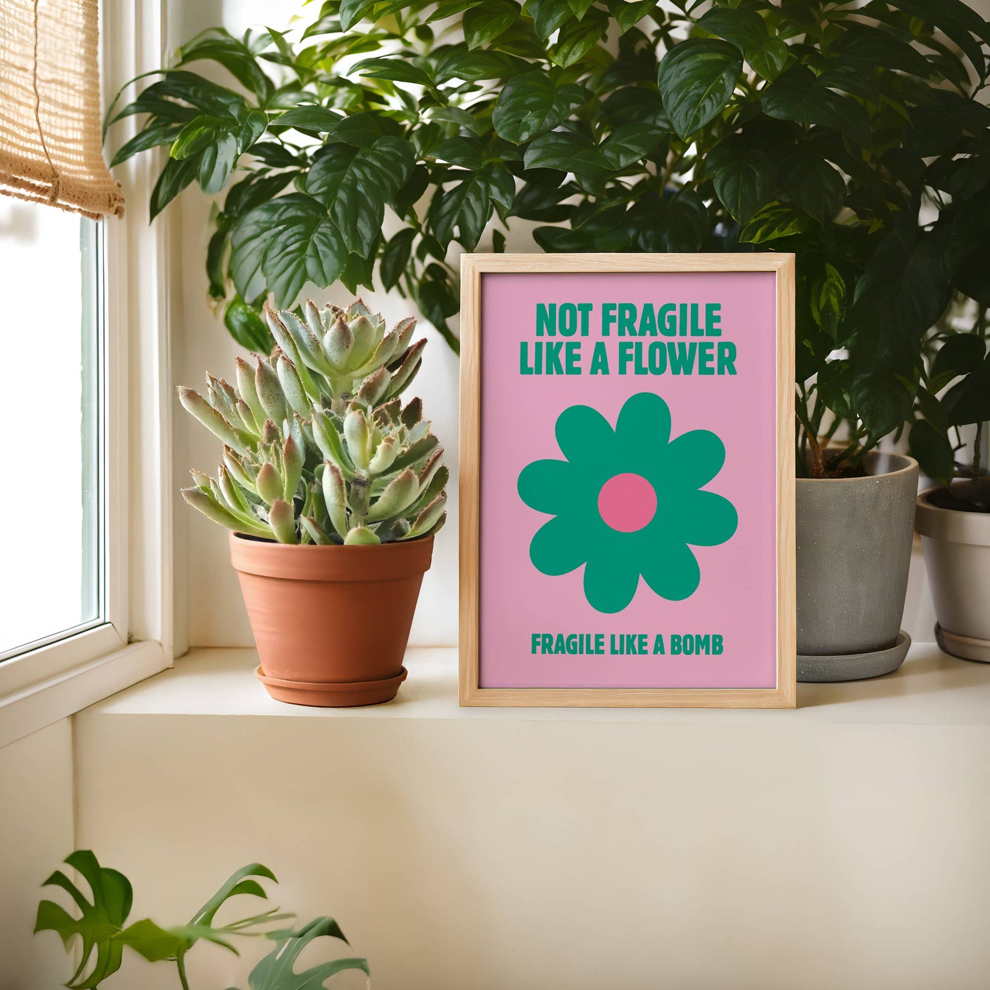 Framed artwork with a flower design and text on a windowsill with plants.