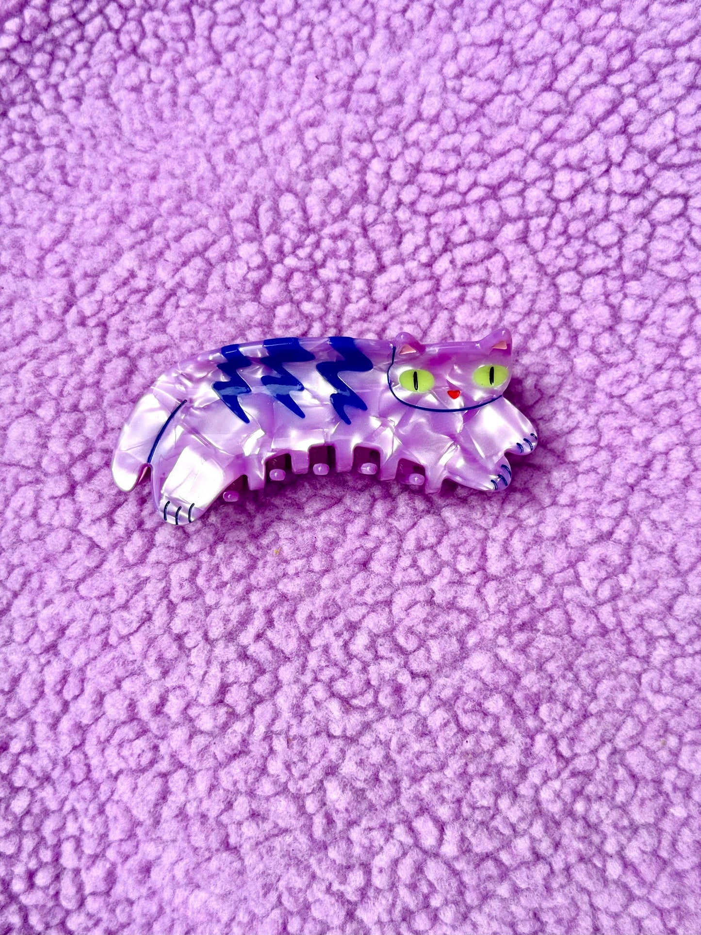 Cat-shaped hair clip with blue and white stripes on a purple textured background