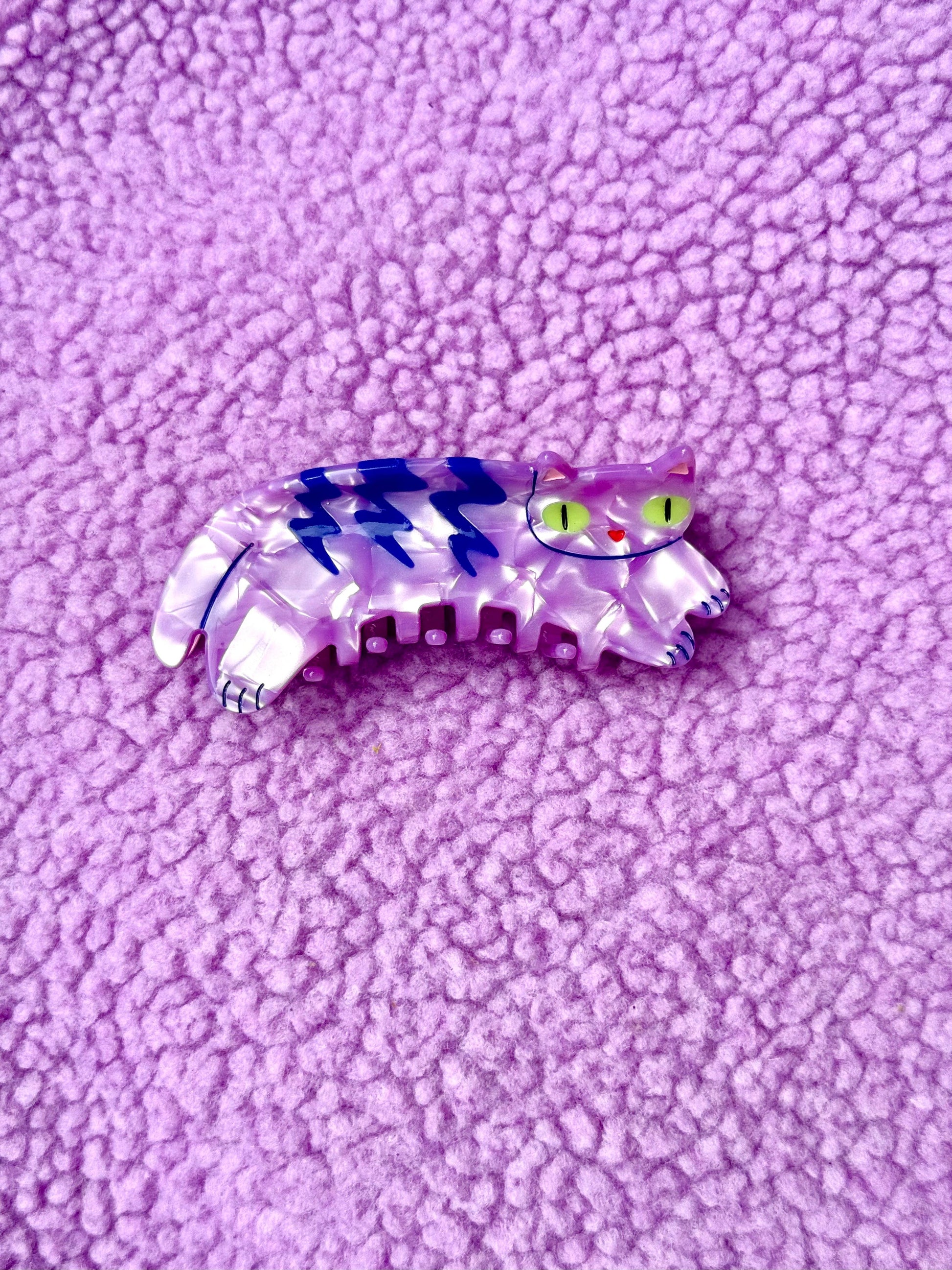 Cat-shaped hair clip with blue and white stripes on a purple textured background