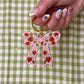 Pink bow keychain with strawberry design held by a hand on a green and white checkered background